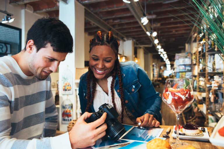 Mixed race couple of photographers looking at a photo camera choosing some photos at the agency while having breakfast
